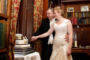 Bride and Groom cutting wedding cake in library setting